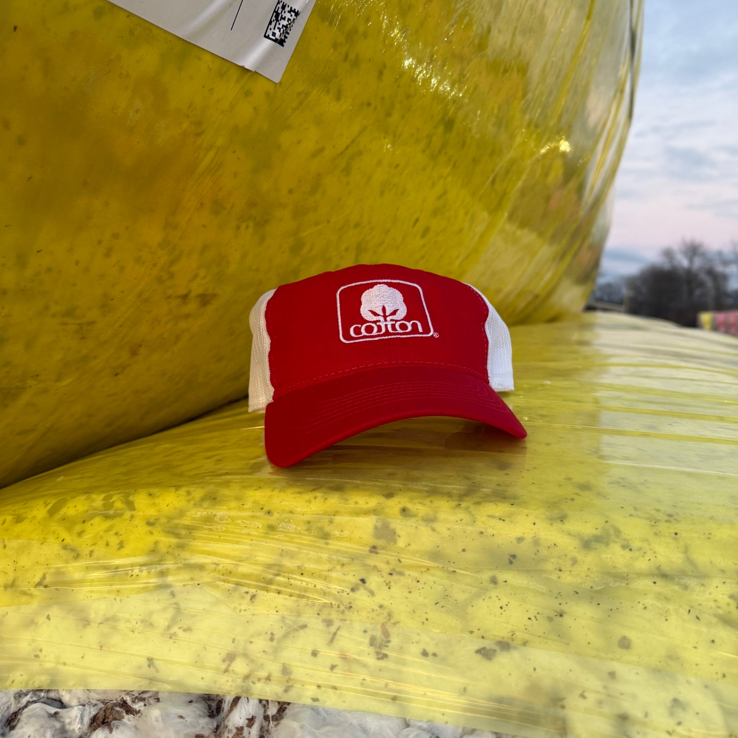 Red and white mesh back hat with adjustable fit and embroidered Seal of Cotton logo