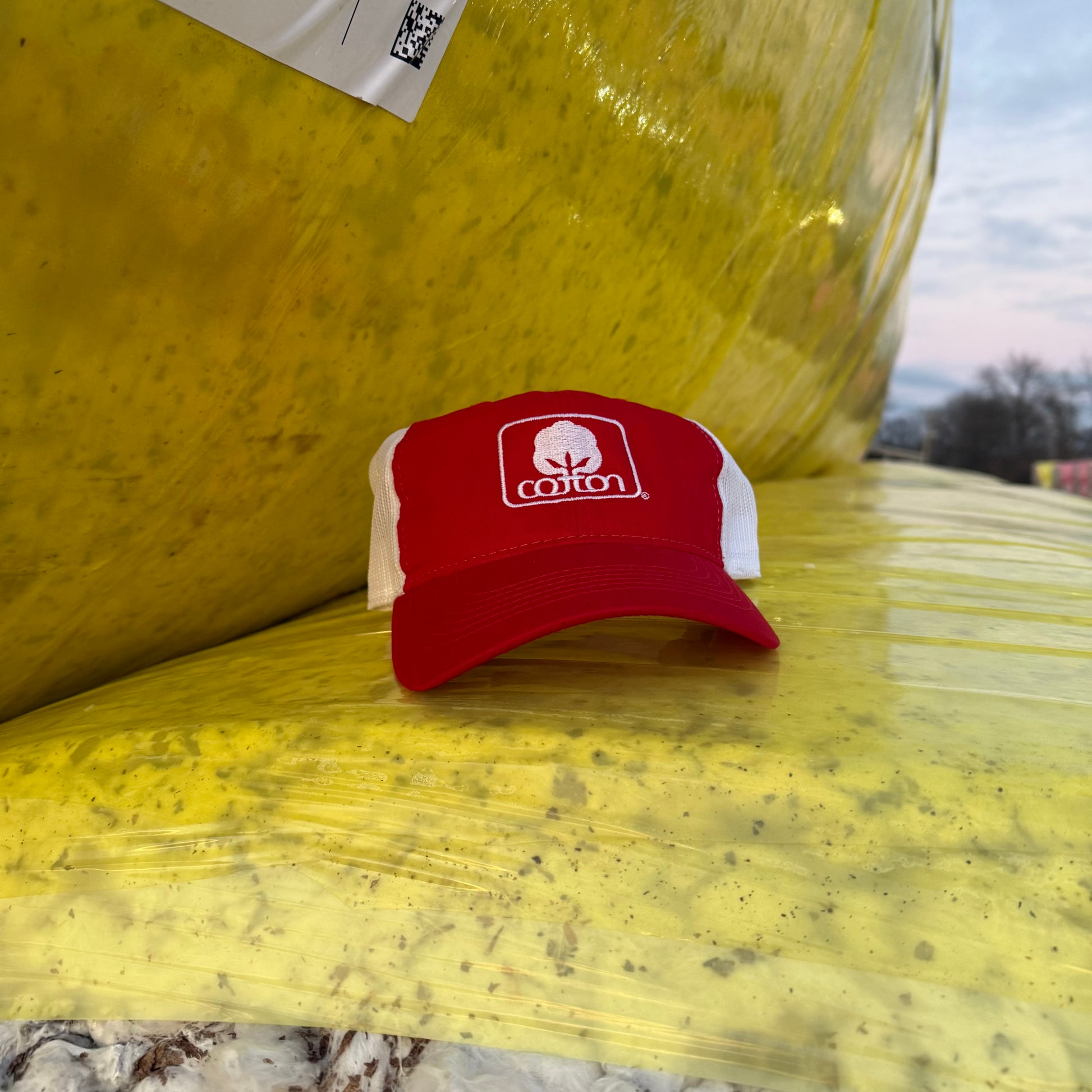 Red and white mesh back hat with adjustable fit and embroidered Seal of Cotton logo
